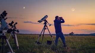 Man uses one of the best telescopes and binoculars to look at the night sky as the sun sets and telescopes are on tripods around him